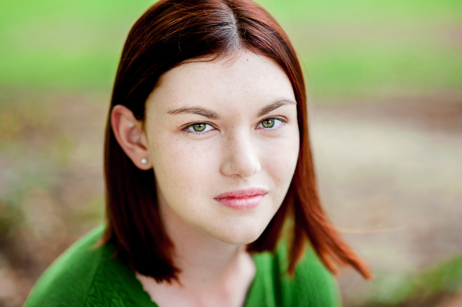 A young woman with red hair and green eyes wearing a green sweater